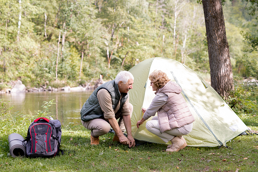 Mature hikers in activewear putting tent