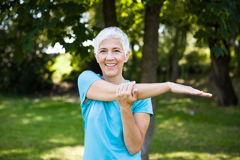 Senior woman exercising tretching arm in the park